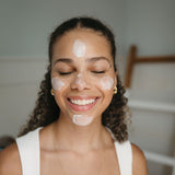 Woman applying cream to her face with a neutral background