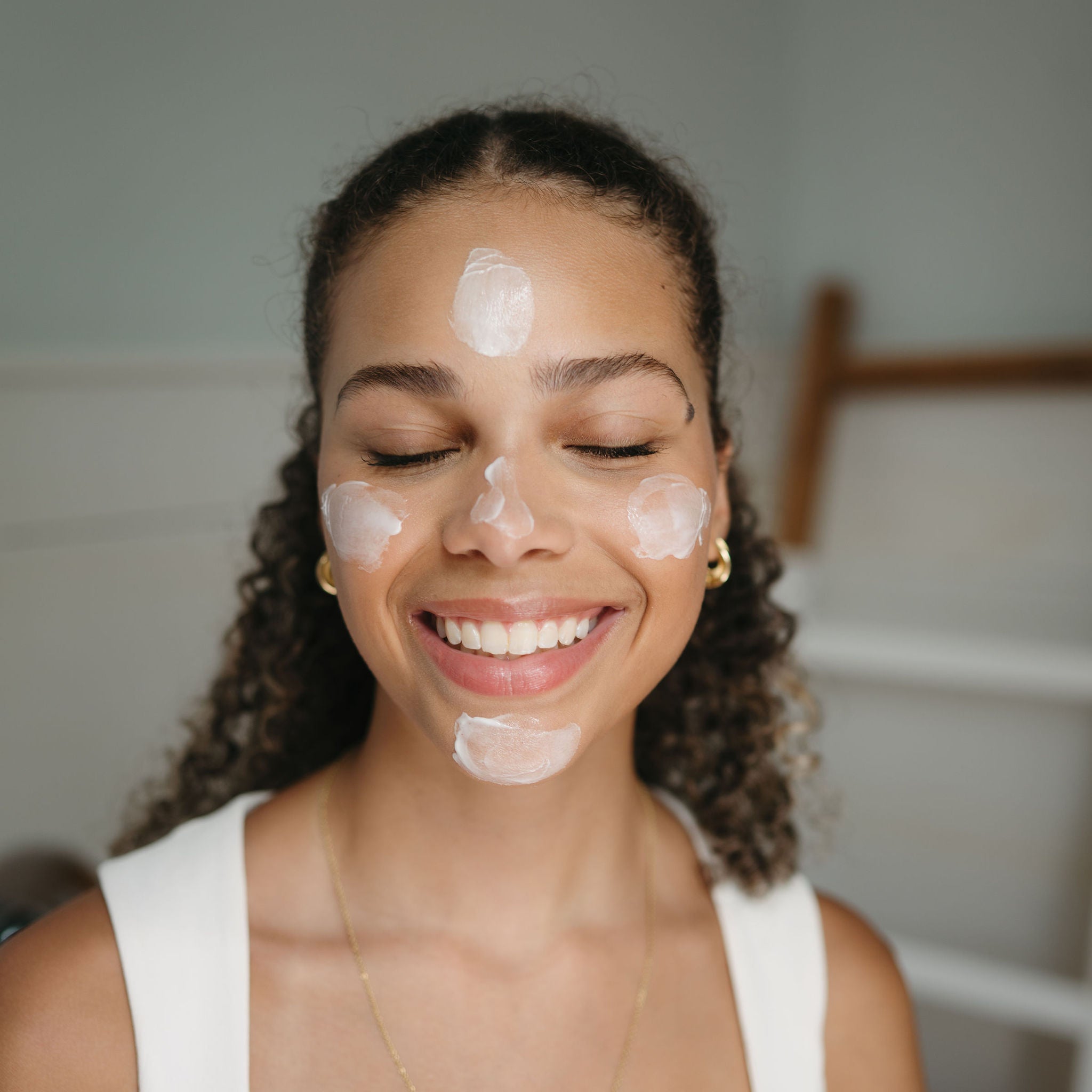 Woman applying cream to her face with a neutral background