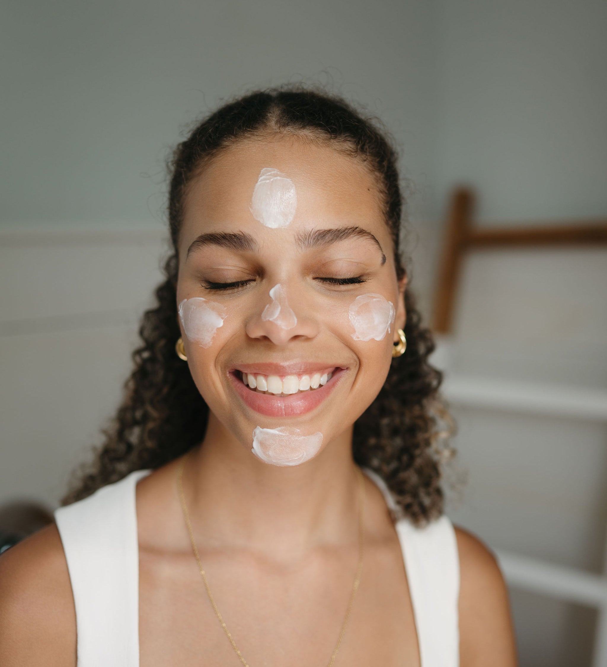 Woman applying cream to her face with a neutral background