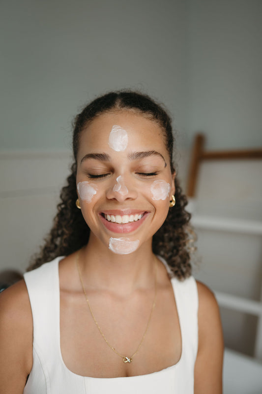 Woman applying cream to her face with a neutral background