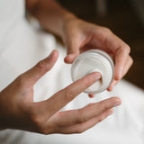Person holding a small container of cucumber aloe moisturizer with a white lid