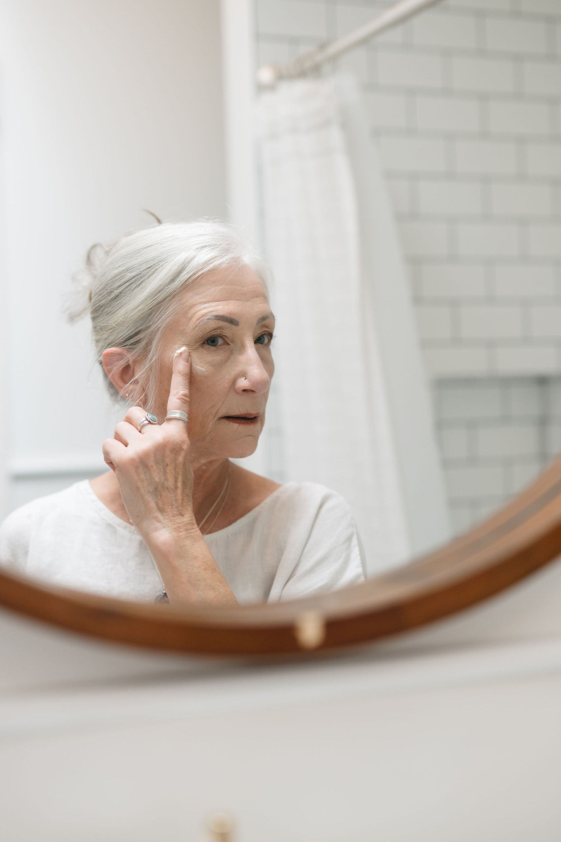 Woman applying skincare product in front of a mirror in a bathroom.