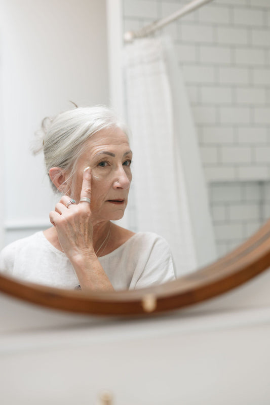 Woman applying skincare product in front of a mirror in a bathroom.