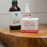Bottle and box of 'wild rose & hibiscus' product on a wooden stool against a tiled wall.