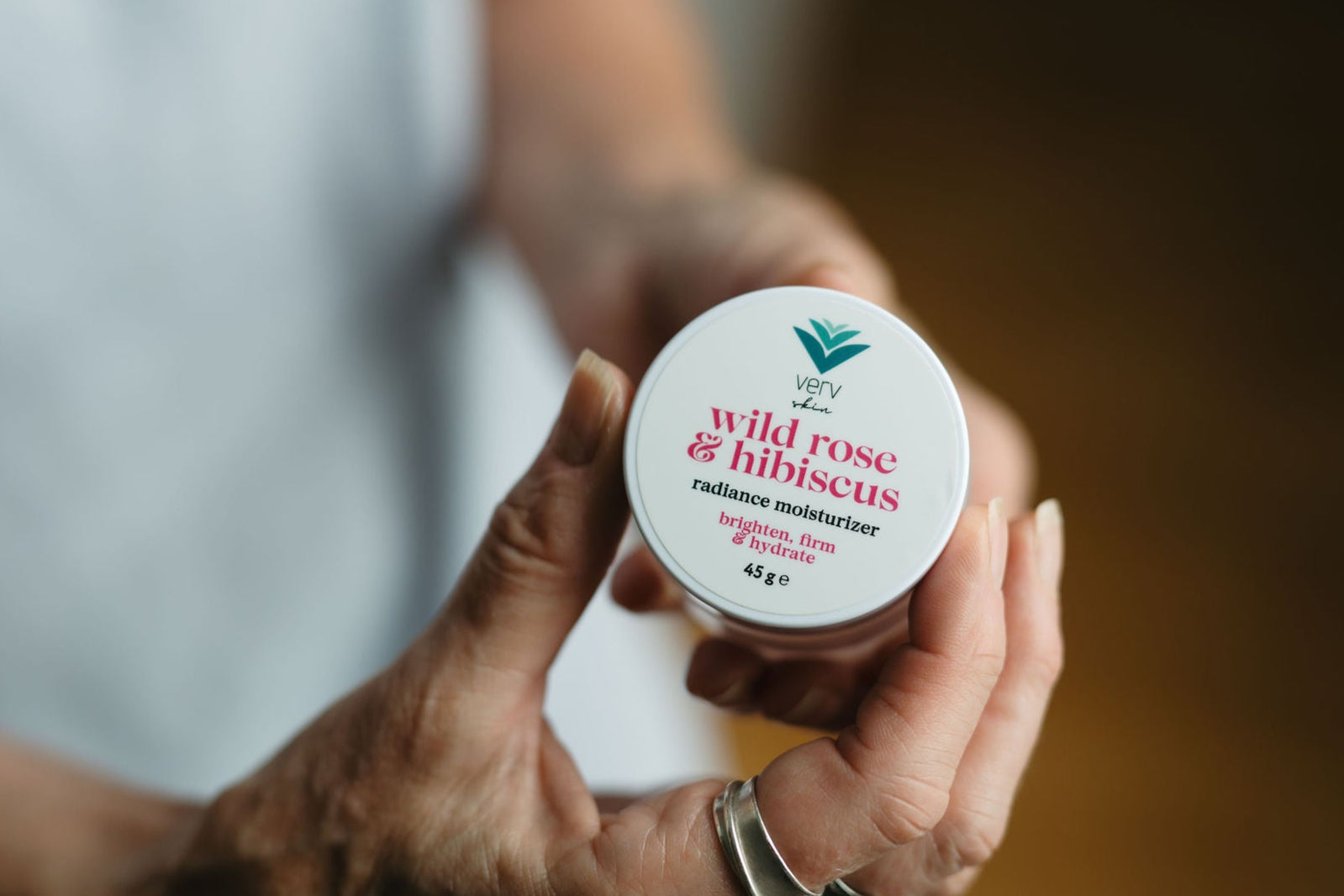 Hand holding a container of 'wild rose & hibiscus' moisturizer by Verv.
