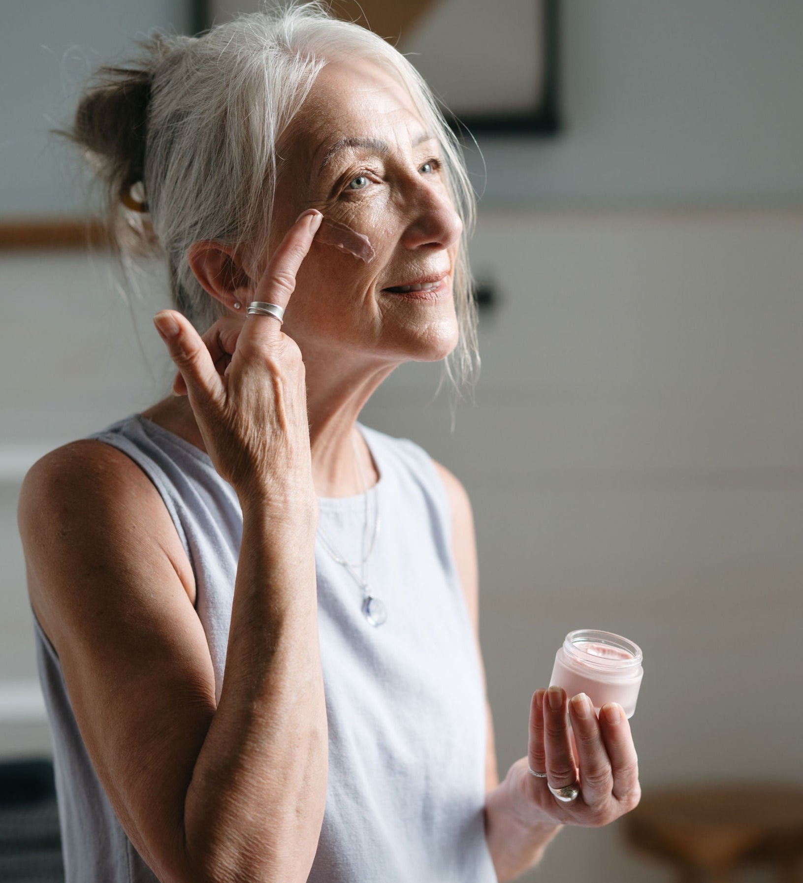 Woman applying cream to her face in a home setting